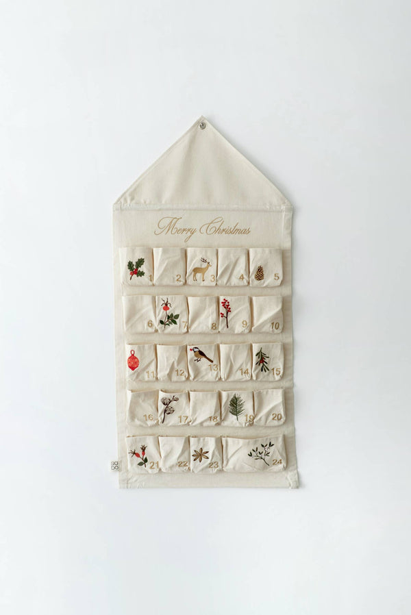 The Sabo Concept Christmas Cotton Advent Calendar is a cream-colored calendar with 24 numbered pockets, each featuring festive embroidery such as holly, birds, and pine branches. "Merry Christmas" is written in gold script at the top.
