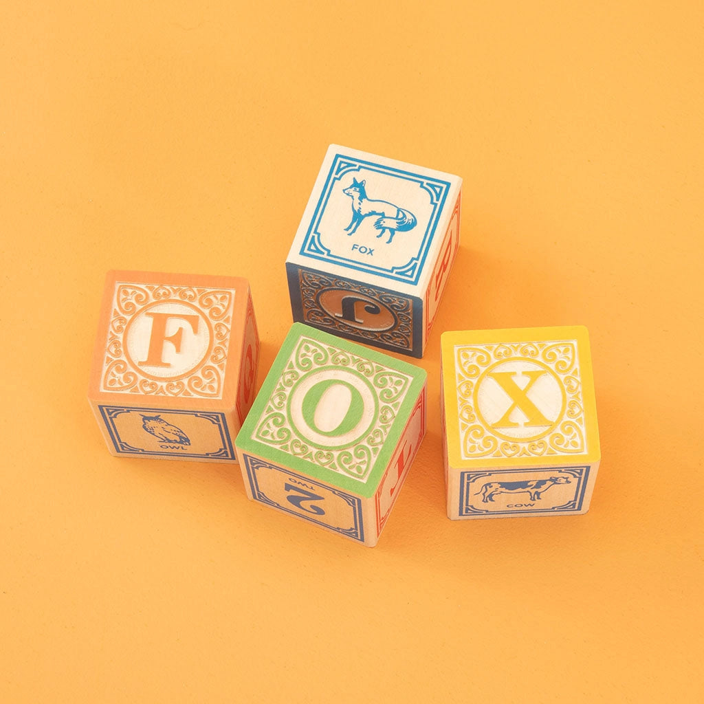 Three Uncle Goose Classic ABC Blocks spelling "fox" with animal illustrations, set against a plain orange background.
