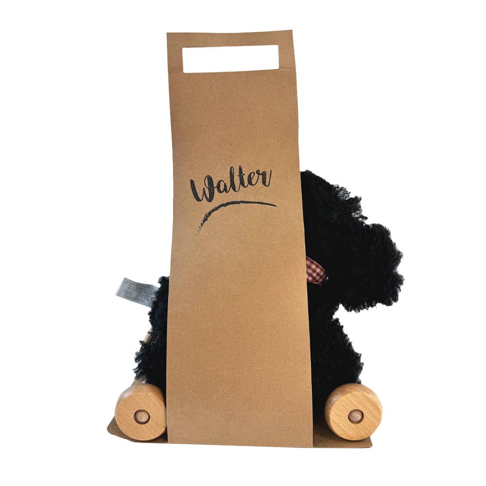 Pull-Along Walter is a black stuffed dog with wooden wheels, designed as an adorable pull-along toy. Partially hidden by a brown paper bag labeled "Walter," only its head and legs peek out.