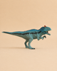 A Schleich Cryolophosaurus Dinosaur Toy with a movable jaw, painted in blue, stands on a beige background with its mouth open and small arms raised.