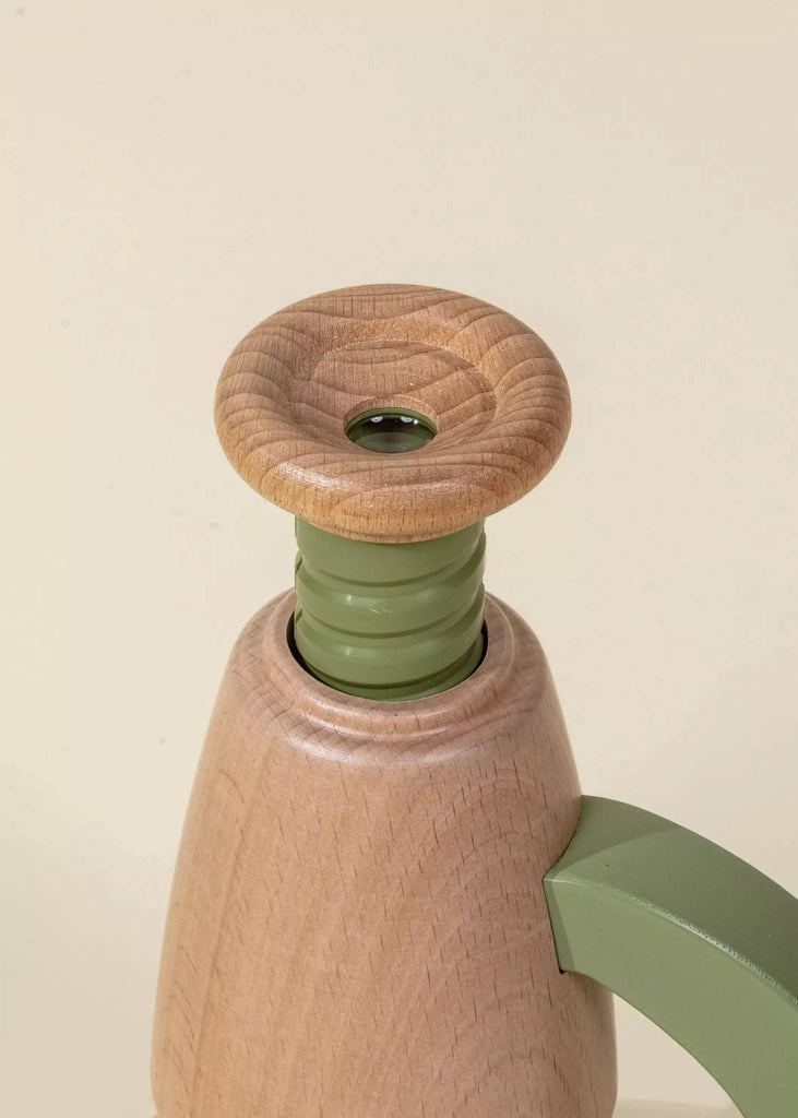 A close-up of the Little Scientist Wooden Microscope, featuring a wooden container with a rounded flat lid and a green plastic neck and handle, set against a plain beige background.