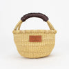 A woven basket with a dark brown leather handle.