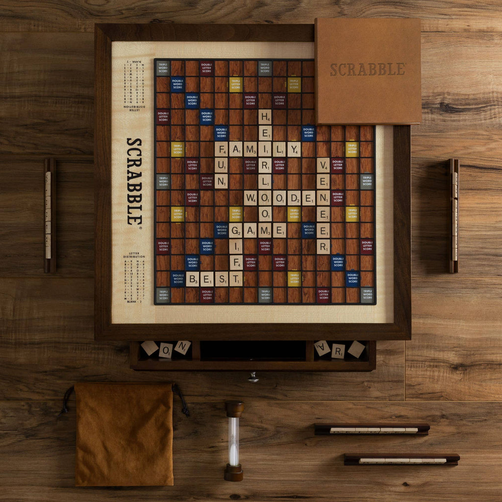 The Scrabble Heirloom with Rotating Game Board features wooden tiles, racks, a sand timer, pouch, and game box—crafted from premium woods for a deluxe experience. Words like “FAMILY” and “WOODEN” decorate the stylish set.