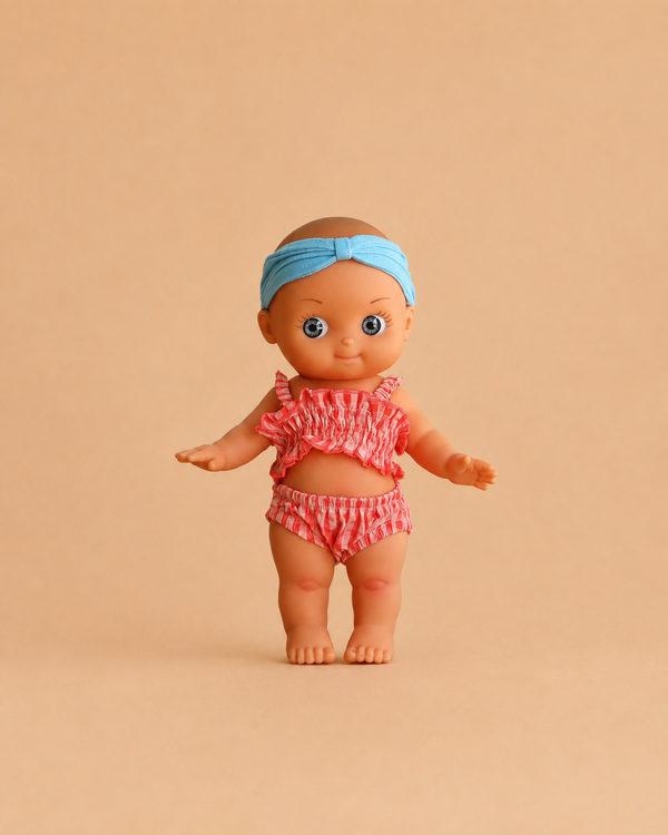 The Minikane Mini Pancha Doll - Alice with Coral Gingham Outfit is a high-quality vinyl doll dressed in a charming coral gingham ensemble, standing on a plain beige background—perfect for inspiring imaginative play.