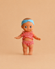 The Minikane Mini Pancha Doll - Alice with Coral Gingham Outfit is a high-quality vinyl doll dressed in a charming coral gingham ensemble, standing on a plain beige background—perfect for inspiring imaginative play.