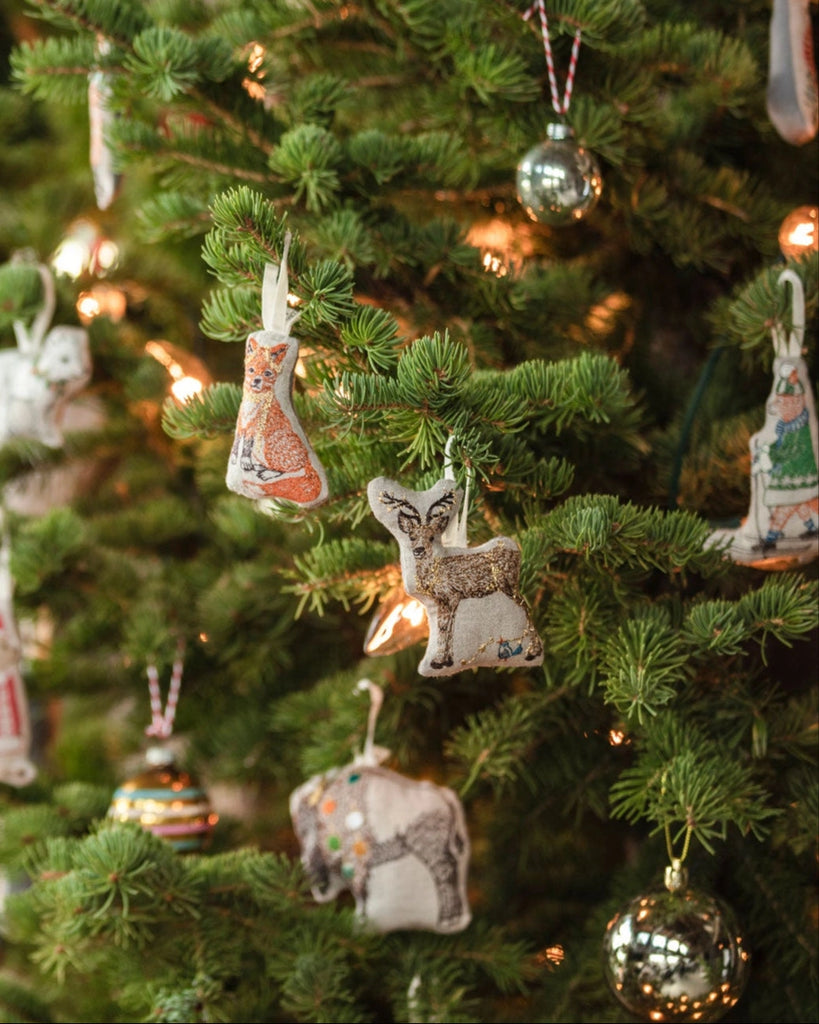 A decorated Christmas tree displays the Coral & Tusk Deer with Lights Ornament alongside a fox ornament, metallic baubles, and glowing string lights.