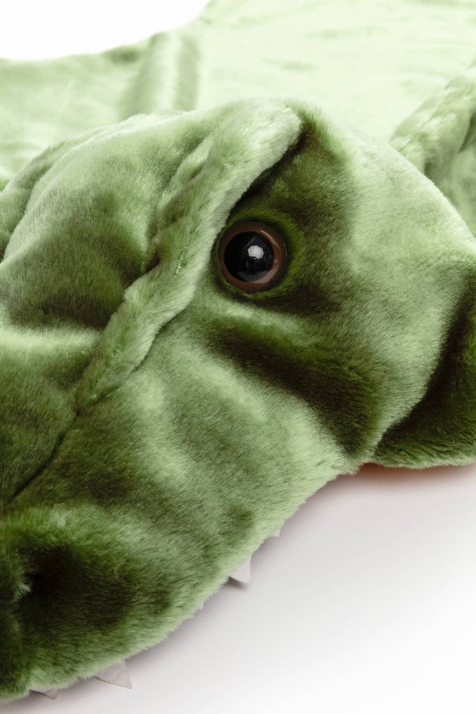 A close-up of a plush green crocodile toy with a shiny black eye and soft faux fur—perfect for pairing with the Costume - T-Rex Dino.