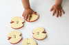 A child’s hands reach for four Pepita the Apple Teething Toys—apple slice-shaped teethers made from natural rubber—safe and designed for sensory play, not real fruit.