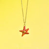 A Starfish Necklace with red speckles, hand painted and hanging from a delicate 24k gold plated steel chain against a soft yellow background.
