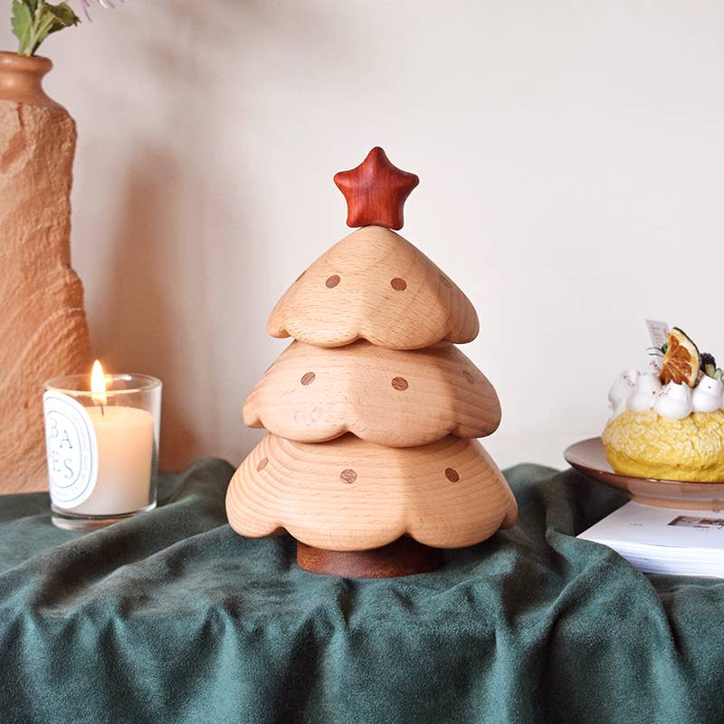 A small wooden Christmas tree with a red star sits on green fabric next to a lit candle and dessert plate—perfect for display or later storage in your Christmas Tree Storage Box.
