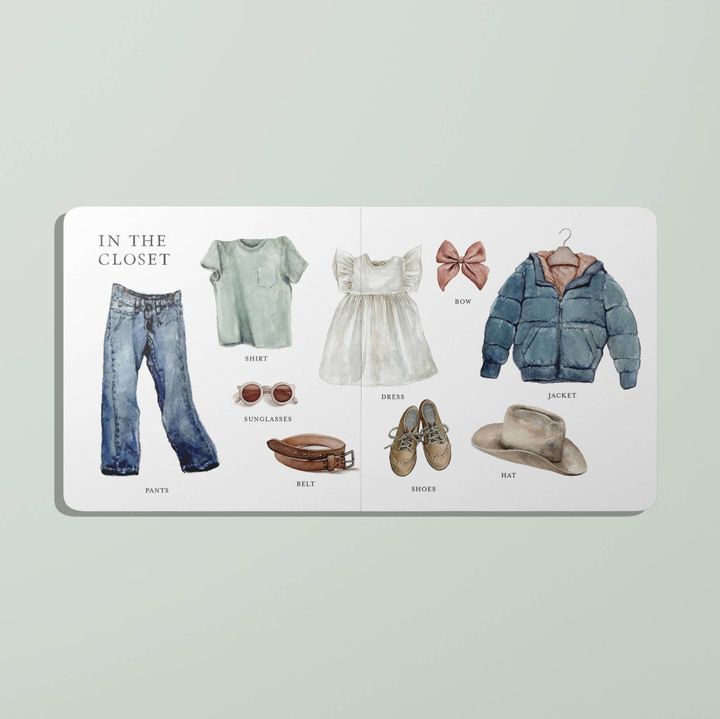 A spread from Our Big Book of First Words shows illustrated clothing—pants, shirt, belt, sunglasses, dress, shoes, bow, jacket, and hat—each labeled on a white background to help little ones learn their first words.