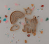 The Unicorn Cutter Set - Eco Playdough Tool features tan plastic cookie cutters in whimsical shapes including a rainbow, star, cloud, and unicorn. Surrounded by vibrant gemstones on a light background, these eco-friendly sensory play tools inspire imaginative creativity with the unique unicorn cutter included in the set.