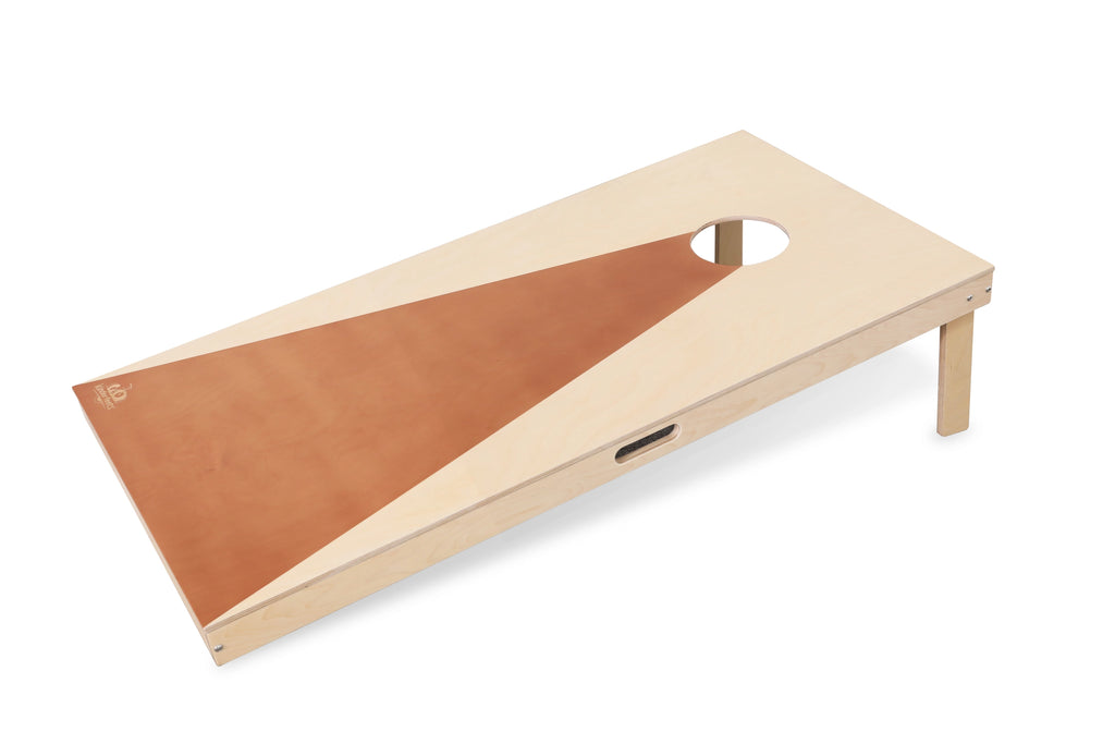 A Cornhole Game with a modern, minimalist design features a triangular light brown section extending from the bottom left corner to the top near a circular hole. The board has foldable legs and a handle for portability, and it comes with all-weather bean bags for your cornhole game.
