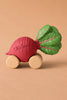 Betty The Beetroot Baby Car, made from FSC-certified wood and natural rubber, features four wooden wheels, green leaves, and "Olli Ella" on its red body. It’s displayed against a plain beige background.