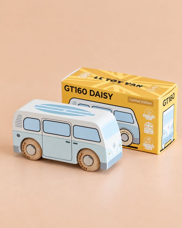 A blue and white vintage-style wooden campervan toy sits in front of a yellow box labeled “No. 29 GT160 Daisy” and “Made in England” on a beige surface. The box features an illustration that matches the retro design of the toy.