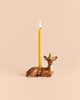 The Deer Cake Topper - Final Sale (ships in one week) features a ceramic deer with a striped party hat holding a yellow candle—an adorable, hand-painted birthday decoration against a beige background.