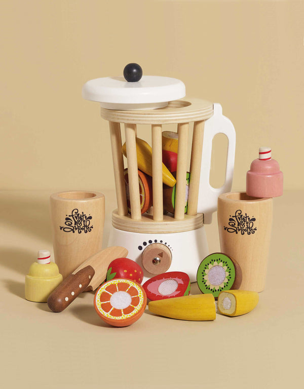 The Fruit & Smoothie Blender Set includes a wooden toy blender, sliceable apple, kiwi, banana, and orange pieces, two cups, a knife, and bottles—ideal for any toy kitchen. Displayed on a beige surface with a beige background.