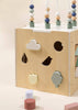 The Wooden Activity Cube features shaped cutouts and matching blocks—cloud, tree, tulip, circle, bird—plus colorful wire beads to develop fine motor skills. Loose geometric blocks are included for added play.