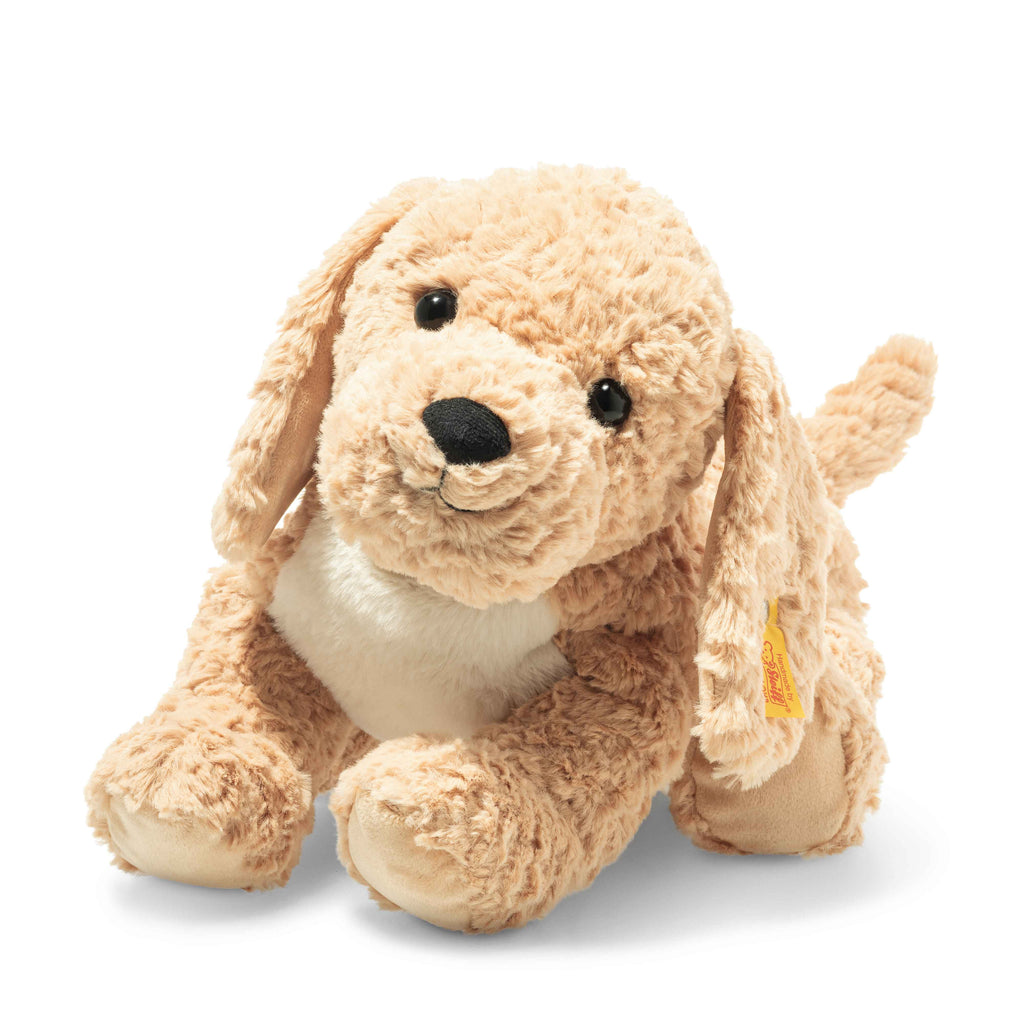 The Steiff Berno Goldendoodle Dog Plush Stuffed Animal, with light brown fur, floppy ears, and a black nose, sits against a white background. Its cuddly soft fur is complemented by shiny, expressive eyes.