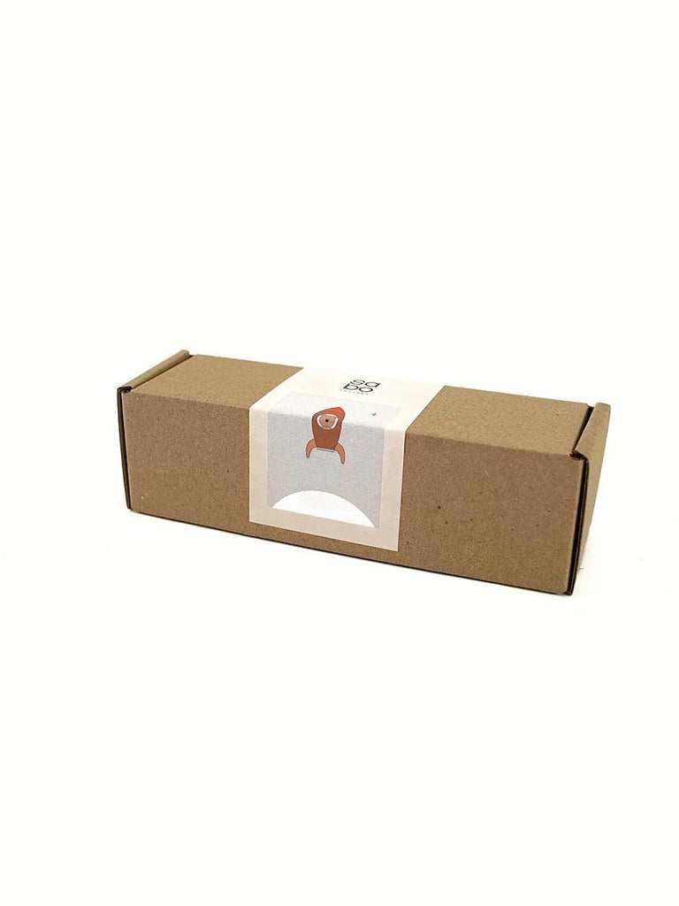 The Sabo Concept Rocket with Bear comes in a small brown rectangular box with a white label featuring a simple brown bear illustration. The sealed box is perfect for imaginative play and rests on a crisp white background.