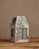 The Coral & Tusk Haunted House Tissue Box Cover, shaped like a house with embroidered pumpkins, skulls, and vines, sits on a wooden surface against a beige wall.