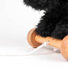 A close-up of a wooden wheel attached to Pull-Along Walter, a fluffy black pull-along toy, on a white background with a white pull string visible in the foreground.