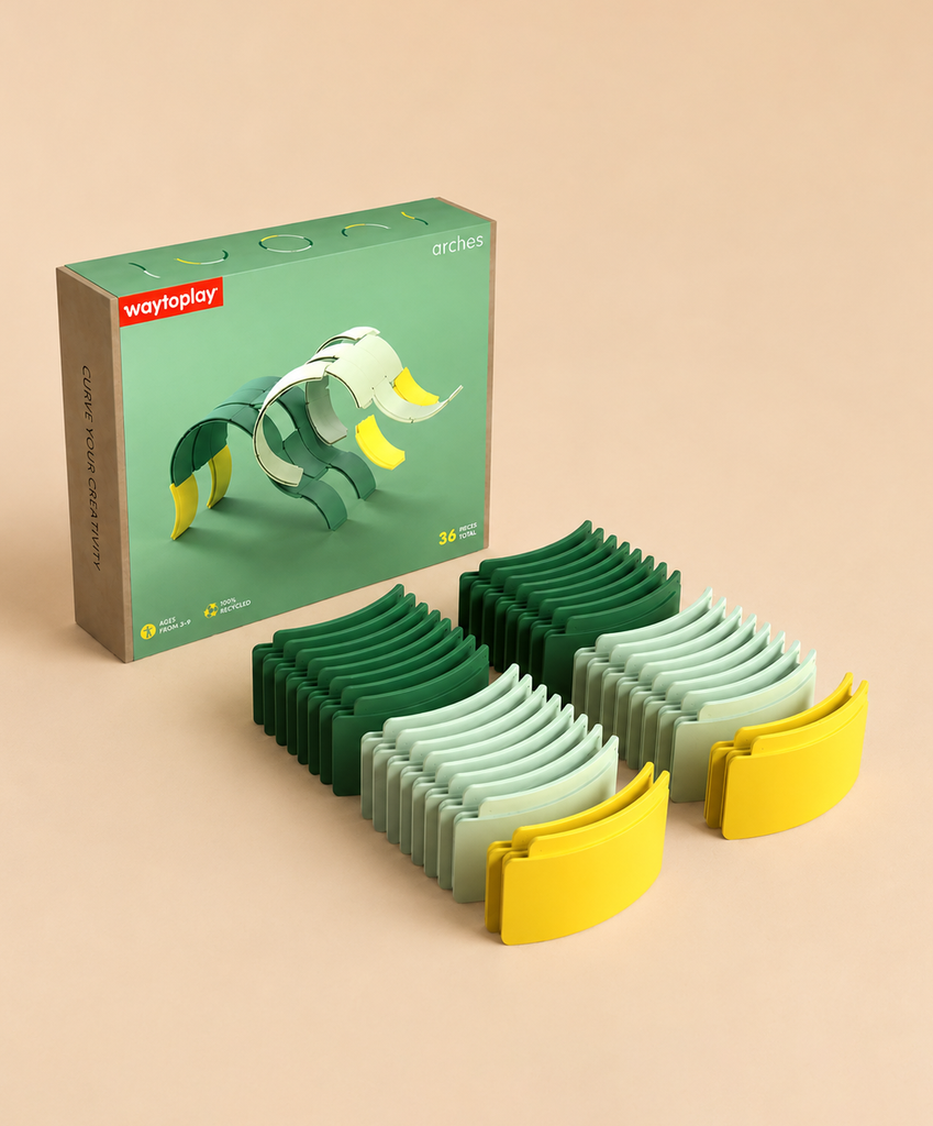 A boxed set labeled “WaytoPlay: Arches - Creator Set” is displayed alongside rows of curved toy pieces in green, light green, and yellow, neatly stacked in three piles on a beige surface. This innovative building set encourages endless play possibilities and serves as an ideal sustainable construction toy for imaginative minds.