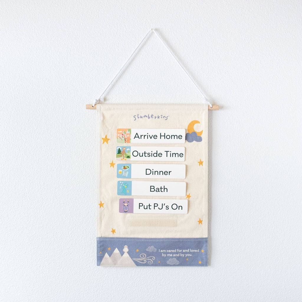 A fabric wall chart for children, titled "Routines Visual Schedule," serves as a visual routine schedule with pockets displaying kids' habits: Arrive Home, Outside Time, Dinner, Bath, and Put PJ's On. Decorated with stars and a moon, it reads "I am cared for and loved by me and by you.