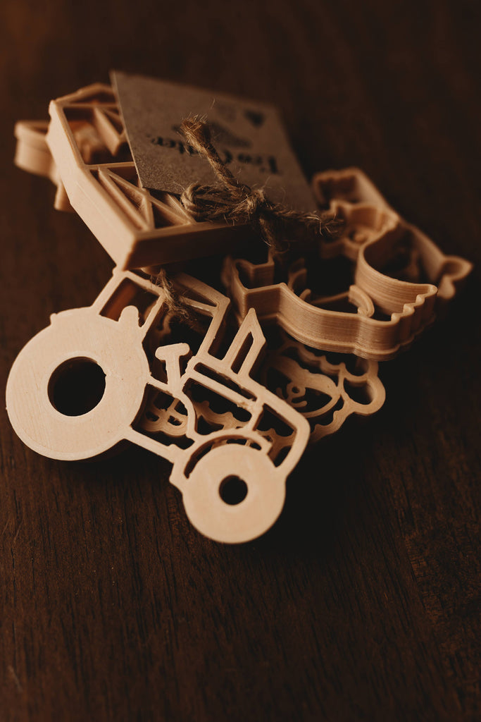 Farm Cutter Set - Eco Playdough Tool: A wooden tractor-shaped ornament featuring intricate cutouts, tied with string and a small cardboard tag, resting on a dark wooden surface—an ideal companion to your Farm Cutter Set - Eco Playdough Tool for inspiring creative sensory play.