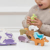 A young child plays with the Woodland Stacking Forest Animals & Bag, stacking colorful wooden animal pieces on a table. Nearby sits a cloth bag decorated with woodland animal prints. The child smiles and holds a green bird from the set. This sustainable toy encourages creativity and imaginative play.