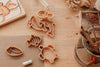 The Under The Sea Cutter Set - Eco Playdough Tool features wooden animal cookie cutters—including a turtle, fish, and dolphin—displayed on a wooden table alongside art supplies, a glass jar with paintbrushes, a piece of chalk, coral, and a starfish drawing. These ocean-themed cutters are perfect for creative and eco-friendly crafting fun.