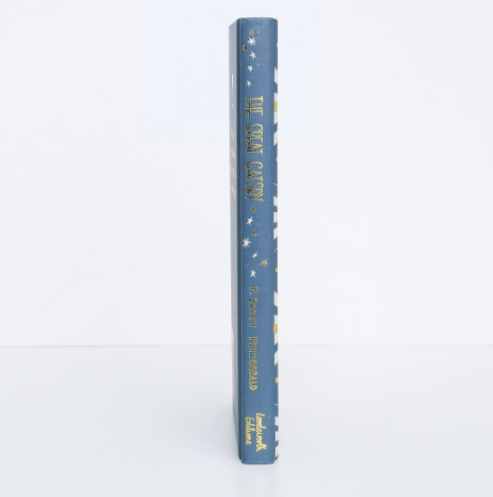 A blue hardcover Collector's Edition of "The Great Gatsby" stands upright with its spine facing forward, displaying yellow and white stars and text on a plain white background—ideal for fans of classic American literature.