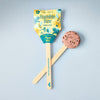 A Pollinator Seed Pop (Single), featuring packaging and a round seed ball on a wooden stick labeled "Wildflowers for Bees," is displayed on a light blue textured surface—ideal for starting your pollinator garden.