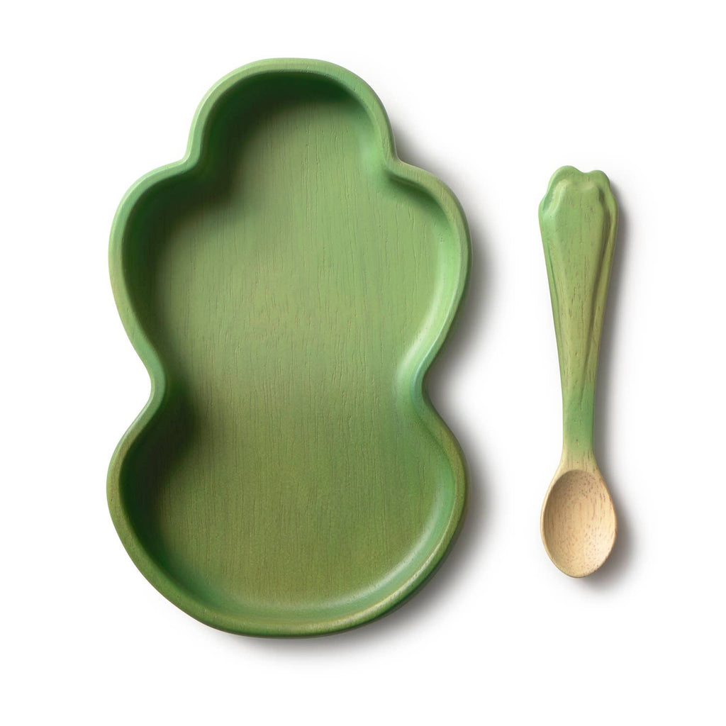 The Kendall the Kale Plate & Spoon Set is a green, frog-shaped baby dinnerware set featuring a non-toxic plate made from sustainable Hevea wood and a matching green spoon with a leaf-like handle—both elegantly displayed on a white background.
