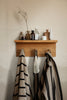 The Ferm Living Place Rack - Small, styled with bottles, jars, and vases on top and three striped towels plus a mesh bag hanging below, is perfect for chic home organization against a beige wall.