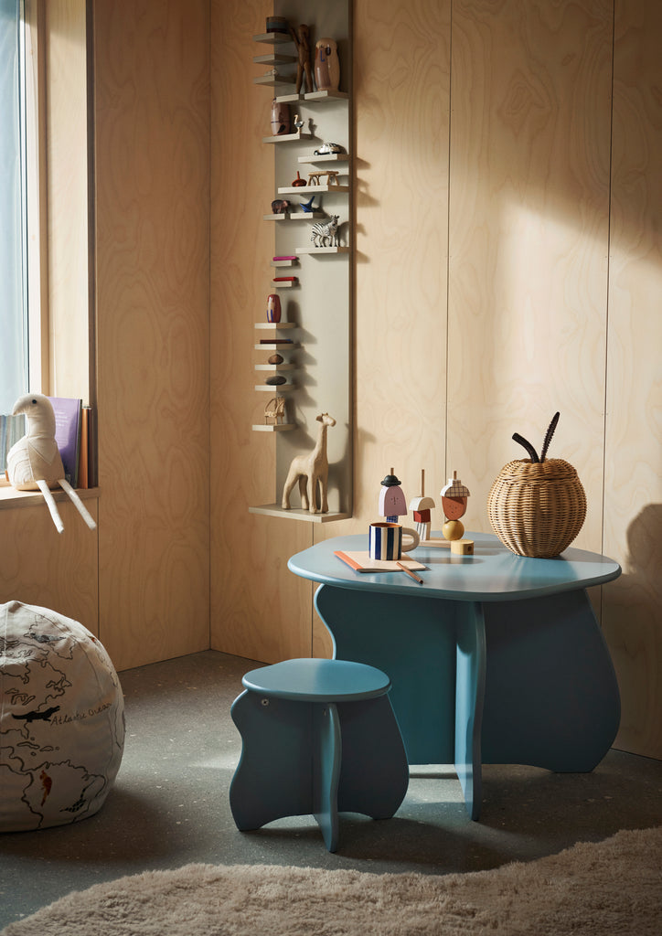 A cozy corner of a room with wooden walls, featuring a blue table and matching stool made from FSC™ certified MDF, an assortment of small toys on the table, and a Ferm Living Parade Shelf - Cashmere.