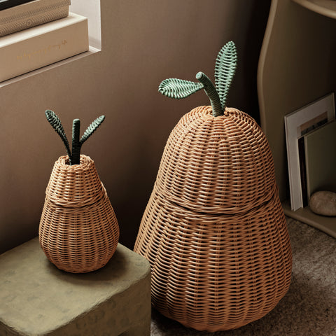 Two Ferm Living Pear Braided Storage Baskets, one large and one small, placed in a cozy kids’ room corner with books and a concrete stool.