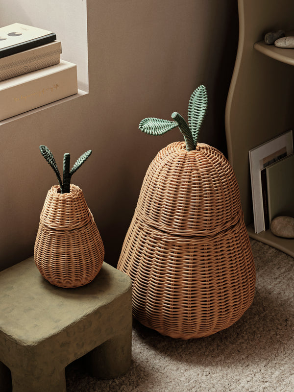Two Ferm Living Pear Braided Storage Baskets, one large and one small, placed in a cozy kids’ room corner with books and a concrete stool.