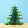 A Bumbu Handmade Wooden Fir Tree from the Bumbu Handmade Wooden Fir Tree Set stands on a light wooden surface against a plain blue background, making it a charming addition to any eco-friendly toy or handcrafted wooden trees collection.