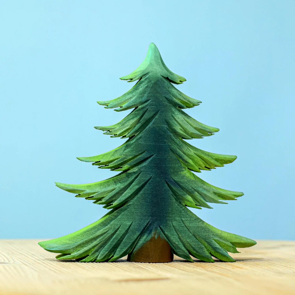 A Bumbu Handmade Wooden Fir Tree from the Bumbu Handmade Wooden Fir Tree Set stands on a light wooden surface against a plain blue background, making it a charming addition to any eco-friendly toy or handcrafted wooden trees collection.