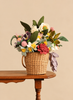 A Basket of Handmade Felt Flowers - Final Sale, featuring a woven basket filled with an everlasting bouquet of colorful handmade felt flowers, sits on a small wooden table.