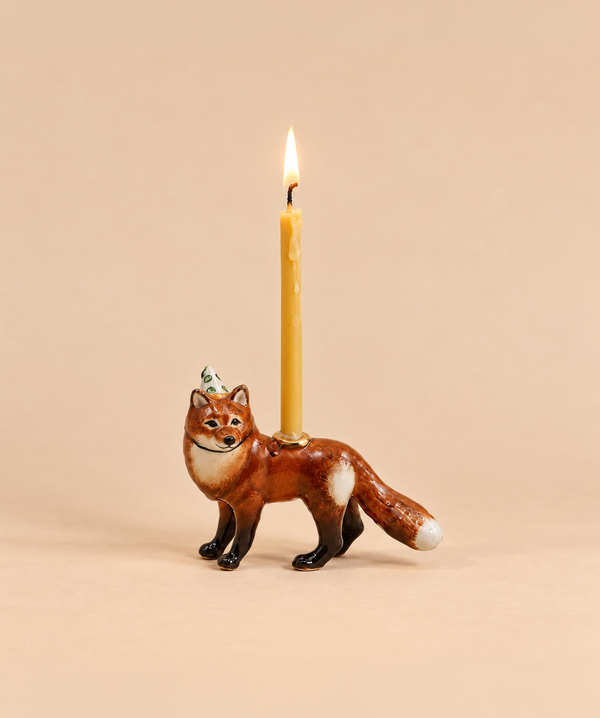 A handcrafted collectible ceramic fox figurine, designed as a “Fox Cake Topper - Final Sale,” features a small burning candle on its back and is set against a plain beige background.