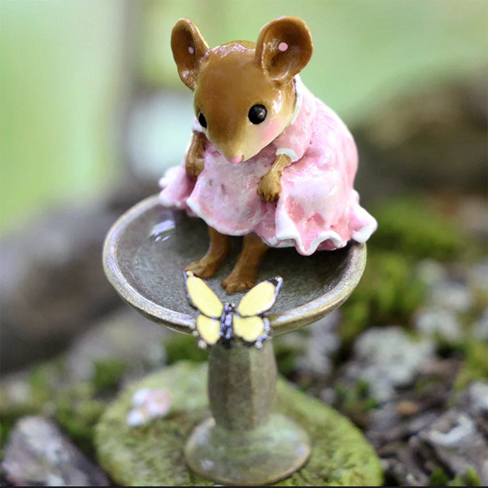 The Wee Forest Folk Tiny Collectible - Garden Spa features a hand-sculpted mouse in a pink dress sitting on a birdbath's edge, admiring a yellow butterfly—an enchanting miniature with an outdoor scene.