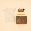 A small star-patterned drawstring bag, a Giraffe Cake Topper - Final Sale with a honeycomb pattern that makes a charming handcrafted collectible, a yellow stick, and a wooden box featuring the “camphollow” name and triangle logo, all arranged on a beige background.