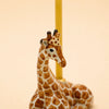 A handcrafted “Giraffe Cake Topper - Final Sale” ceramic figurine with brown spots is lying down, with a yellow candle positioned behind it against a plain, light beige background.