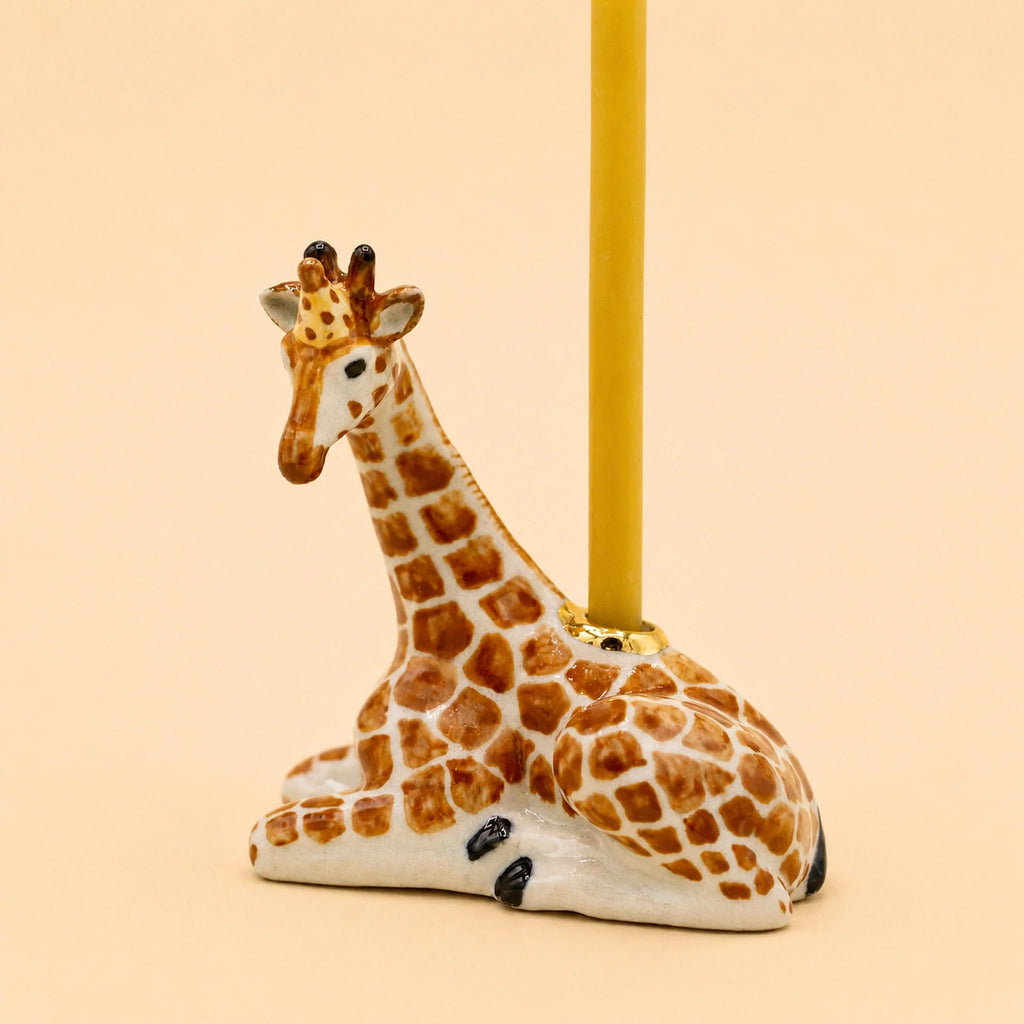 Introducing the Giraffe Cake Topper - Final Sale: a small, handcrafted ceramic giraffe figurine designed to lie down with a candle inserted into a holder on its back—making it the perfect porcelain cake topper or collectible. Photographed against a light beige background.