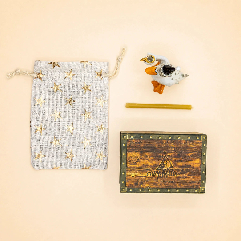 Flat lay of the Goodnight Goose Cake Topper - Final Sale, a star-patterned drawstring bag, a small yellow stick, and a wooden box featuring “camphollow” branding, all arranged on a light beige background.