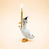 The Goodnight Goose Cake Topper, a handcrafted collectible ceramic figurine featuring a goose wearing a party hat and holding an upright lit candle with one wing, stands out as a charming keepsake birthday decoration against a plain beige background.