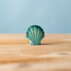 The Bumbu Handmade Wooden Green Seashell toy stands upright on a wooden surface with a blue background, ideal for Montessori-inspired play.