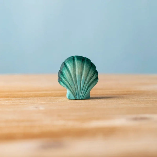 The Bumbu Handmade Wooden Green Seashell toy stands upright on a wooden surface with a blue background, ideal for Montessori-inspired play.
